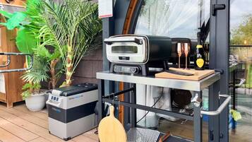A patio area with a grill, a microwave, a portable cooler, and a potted plant.
