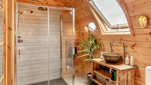 A wooden cabin with a skylight, a glass shower enclosure, a sink with a basin, and a potted plant.