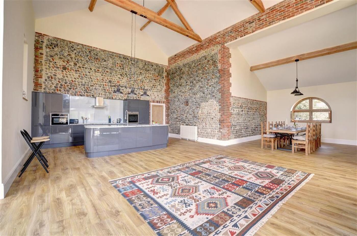 Een ruime loft met zichtbare houten balken, een keuken met moderne apparatuur, een groot tapijt en een eethoek met houten stoelen.