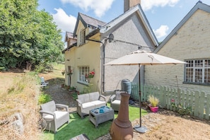 A house with a patio area featuring outdoor furniture, a large umbrella, and a decorative metal vase.