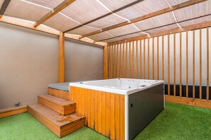 Un bain à remous installé dans un espace extérieur abrité, avec des marches en bois et une pelouse artificielle.