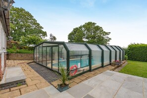 Un invernadero con piscina, rodeado por un patio de ladrillo y un jardín bien cuidado.