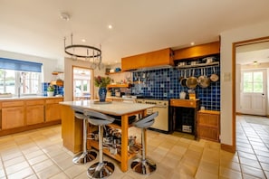 Une cuisine moderne avec des meubles en bois, un îlot central doté de tabourets de bar, une cuisinière et un dosseret de carrelage bleu.
