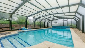 Ein Hallenbad mit großen Glaswänden, Fliesenboden und blauer Beckenumrandung.
