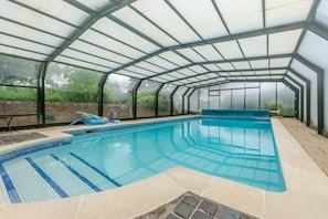 Una piscina interior con paredes de vidrio transparente, suelo de baldosas y borde azul.