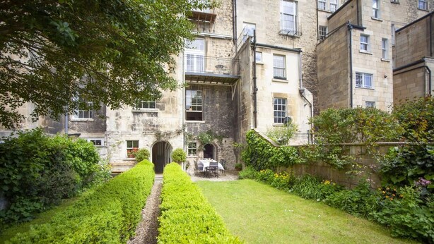 A courtyard with a hedge, a table with chairs, and a building with multiple windows and balconies. - 2 Bed in Bath (oc-bhr35) (Bath)