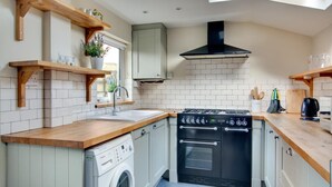 A compact kitchen with a washing machine, a stove, and wooden shelves. - 3 Bed in Cromer (oc-1670) (Cromer)