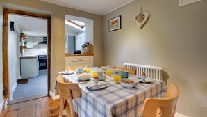 A dining area with a table set for breakfast, a kitchen in the background, and a heart-shaped decoration on the wall. - 3 Bed in Cromer (oc-1670) (Cromer)