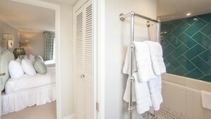 Quarto com cama, porta branca e banheiro com banheira e porta-toalhas.