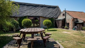 A thatched-roof house with a wooden deck and picnic table. - 2 Bed in Bacton (oc-712) (Bacton)