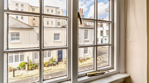 A window with multiple panes, offering a view of a street with buildings and parked cars. - 2 Bed in Brighton & Hove (oc-bbbswe) (Hove)