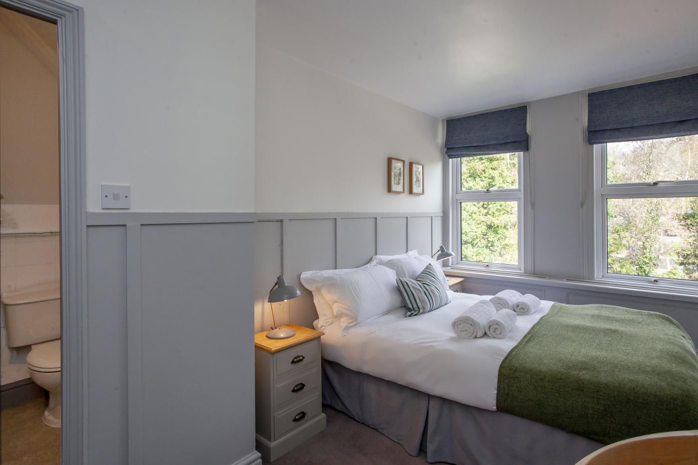 A bedroom with a bed, bedside table, lamp, and a window with a view of greenery.