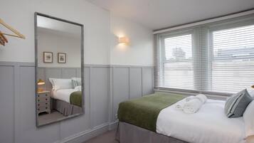 A bedroom with a bed, a bedside table with a lamp, a mirror, and a window with blinds.