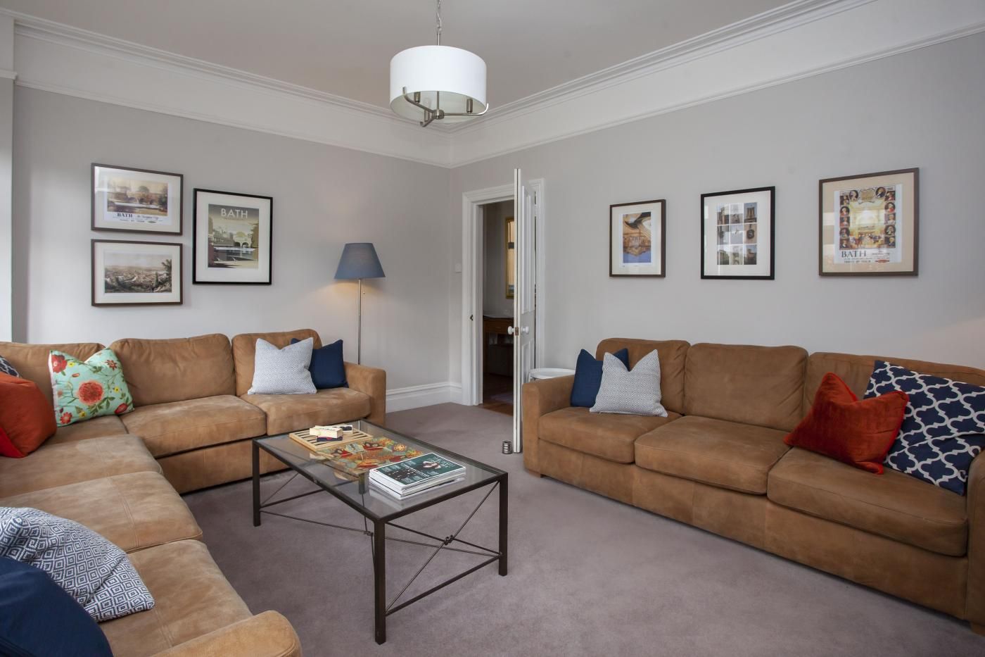 A living room with two brown sofas, a glass coffee table, and framed pictures on the walls.