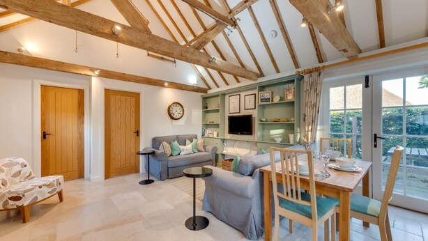 A spacious living area with a high ceiling, wooden beams, a sofa set, a dining table with chairs, and a TV mounted on the wall. - 1 Bed in Maidstone (oc-md435) (Linton)