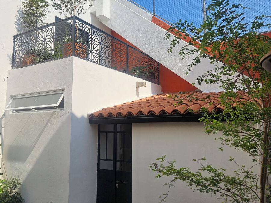 Un edificio de dos pisos con fachada blanca, puerta negra y tejado de tejas.