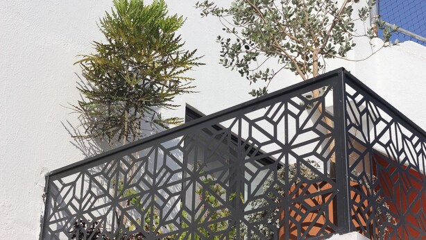 A geometric metal fence, a white wall, and a tree with green foliage. - Casa Mestiza (Guadalajara)