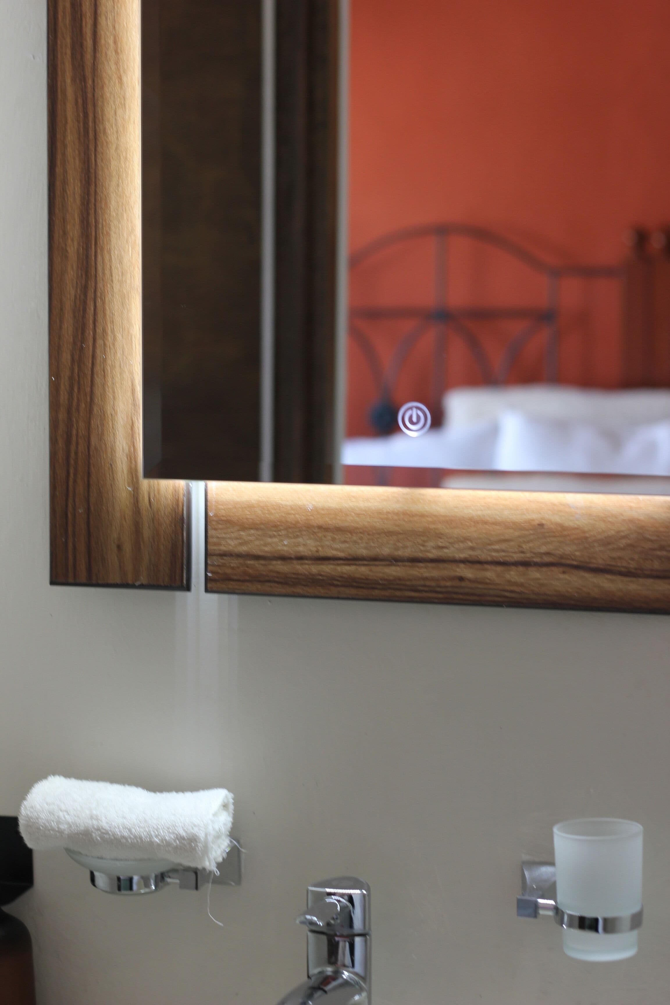 Un baño con un espejo de marco de madera, un perchero, un lavabo y un portavasos de vidrio.