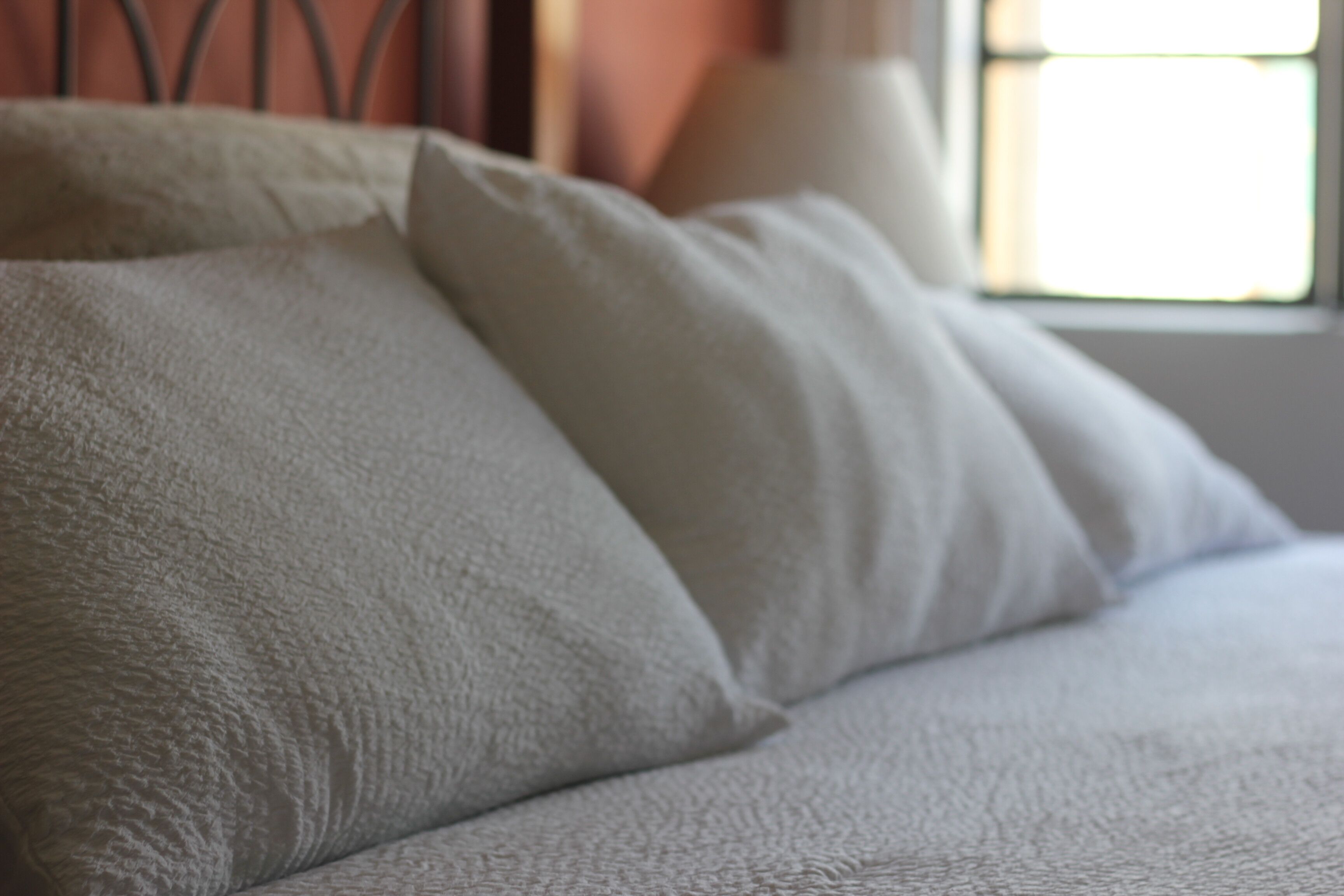 Primer plano de un almohadón blanco con textura sobre una cama.