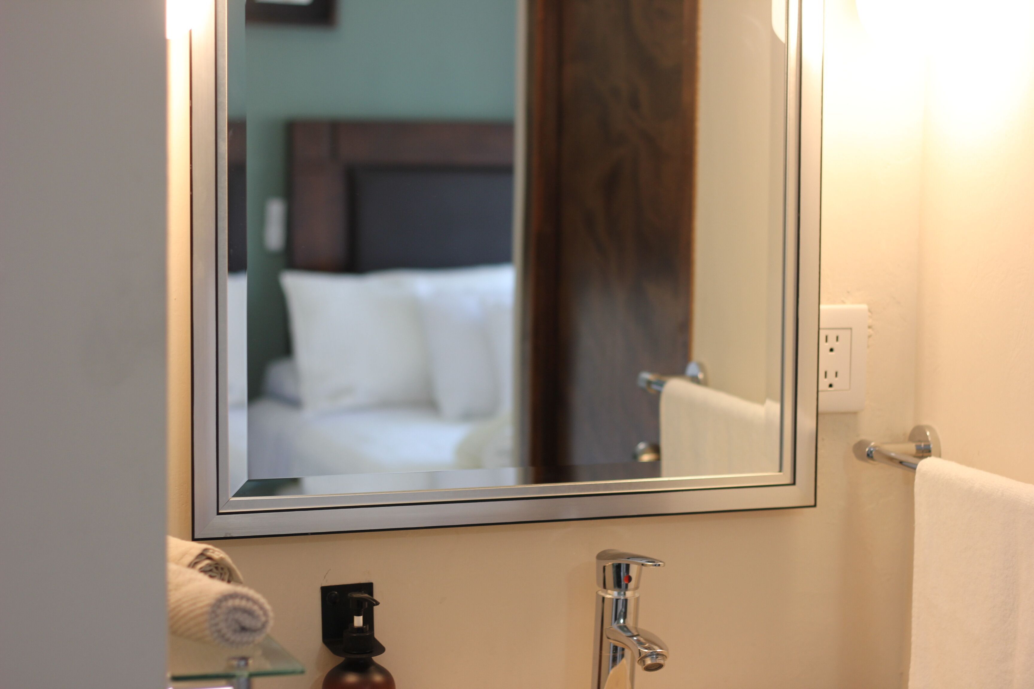A bathroom with a mirror, a towel, a sink, and a showerhead.