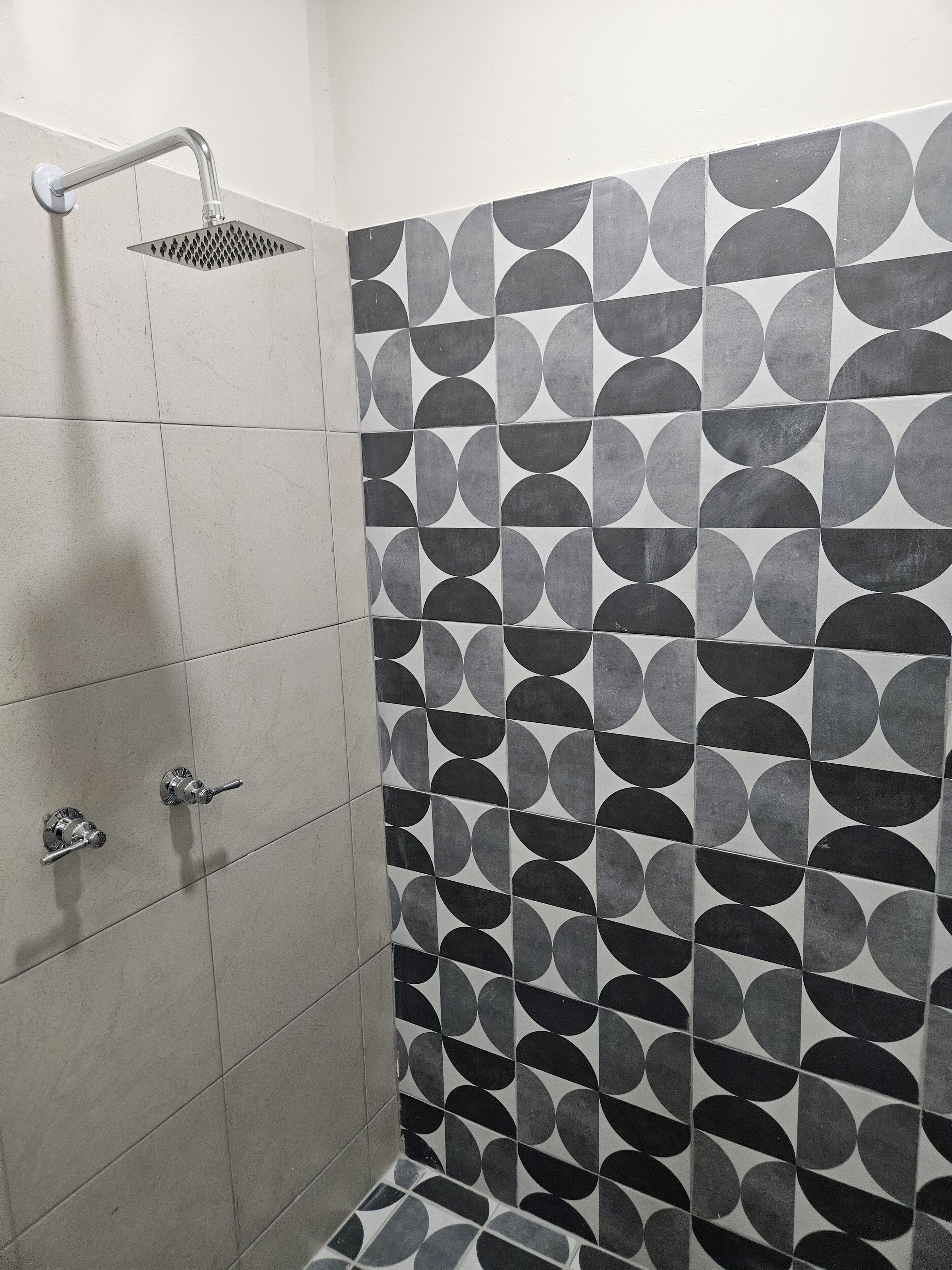 Una ducha con cabezal de ducha de mano, grifo empotrado en la pared y pared cubierta de azulejos con un diseño geométrico.