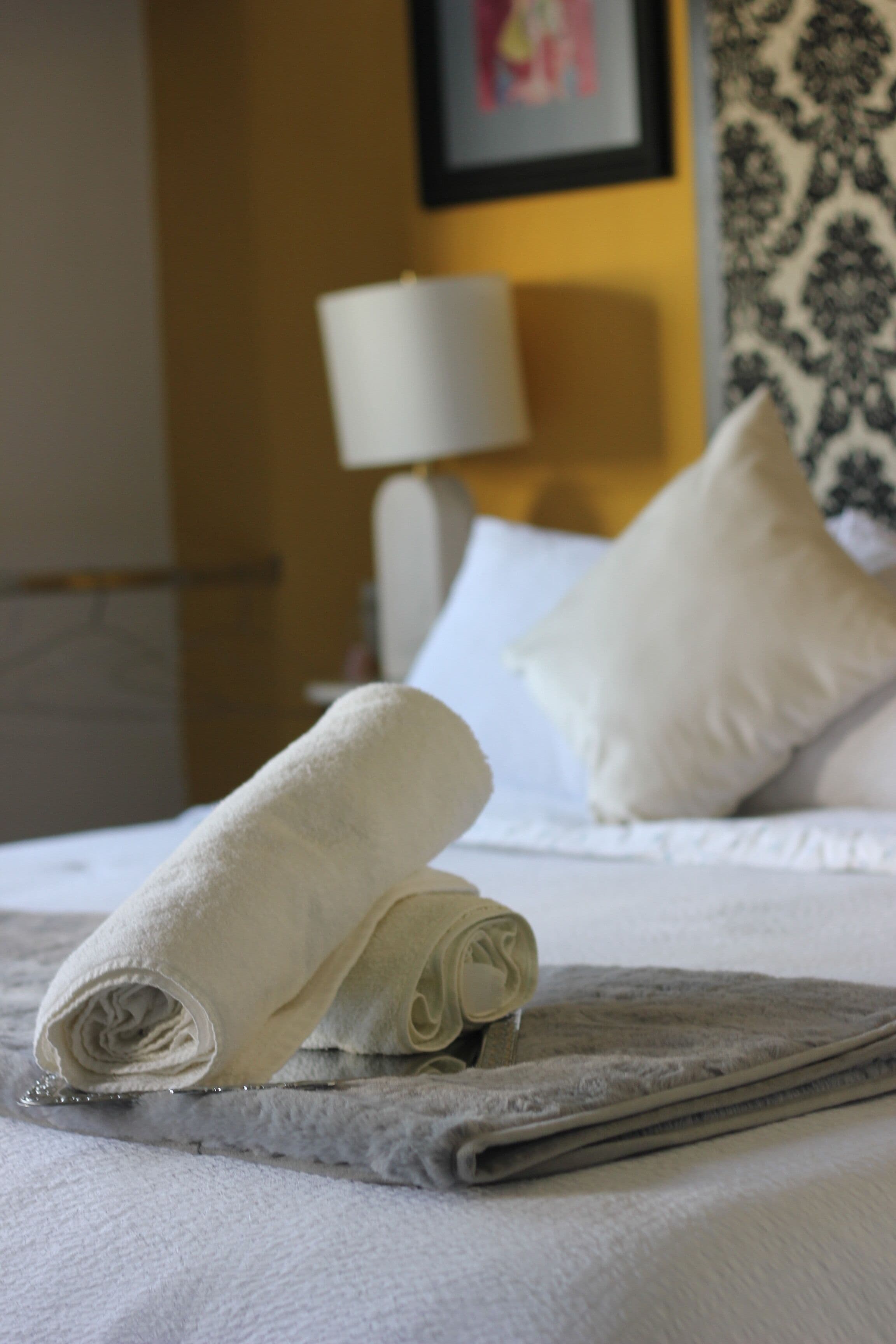 A neatly made bed with a rolled white towel and a folded gray towel.