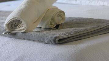 Una cama bien hecha con una toalla blanca enrollada y una toalla gris doblada.