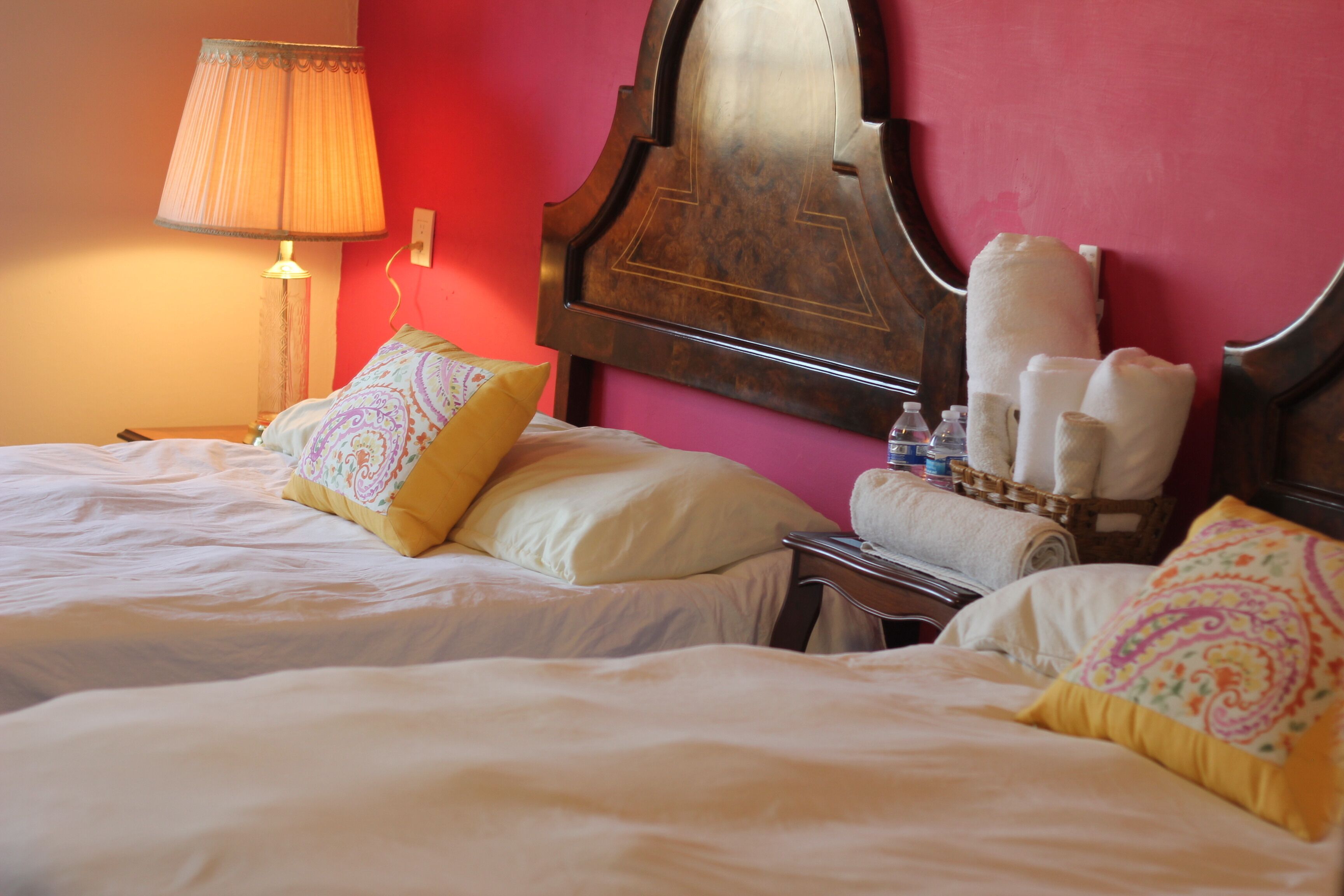 A hotel room with two beds, a lamp, a mirror, and towels on a side table.