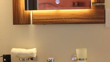 A bathroom with a white sink, a mirror with a wooden frame, a towel hanging on the wall, and a soap dispenser.