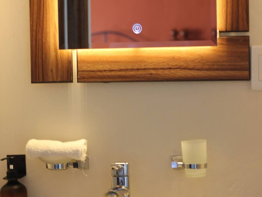 A bathroom with a white sink, a mirror with a wooden frame, a towel hanging on the wall, and a soap dispenser.