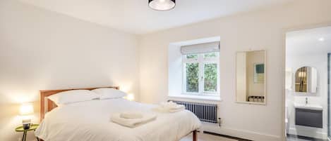 Ein Schlafzimmer mit einem Bett, Nachttischlampen, einem Fenster, einer Heizung und einem durchgehenden Türspalte sichtbaren Badezimmer.