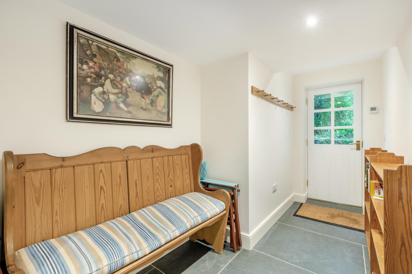 A hallway with a wooden bench, a door with a window, and a framed painting on the wall.