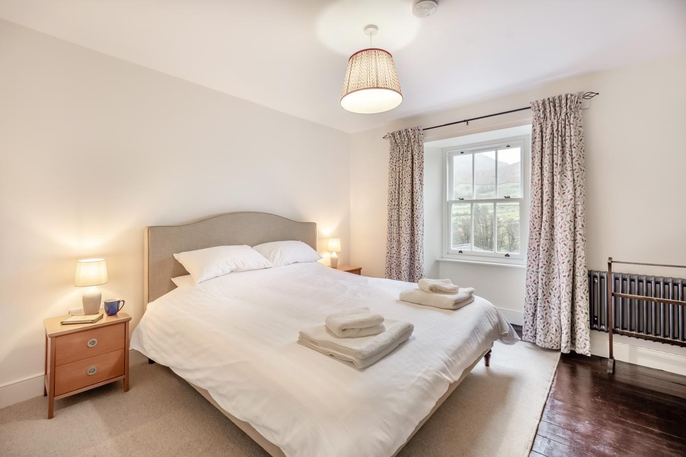 A neatly made bed with white linens, a bedside lamp, and a window with curtains.
