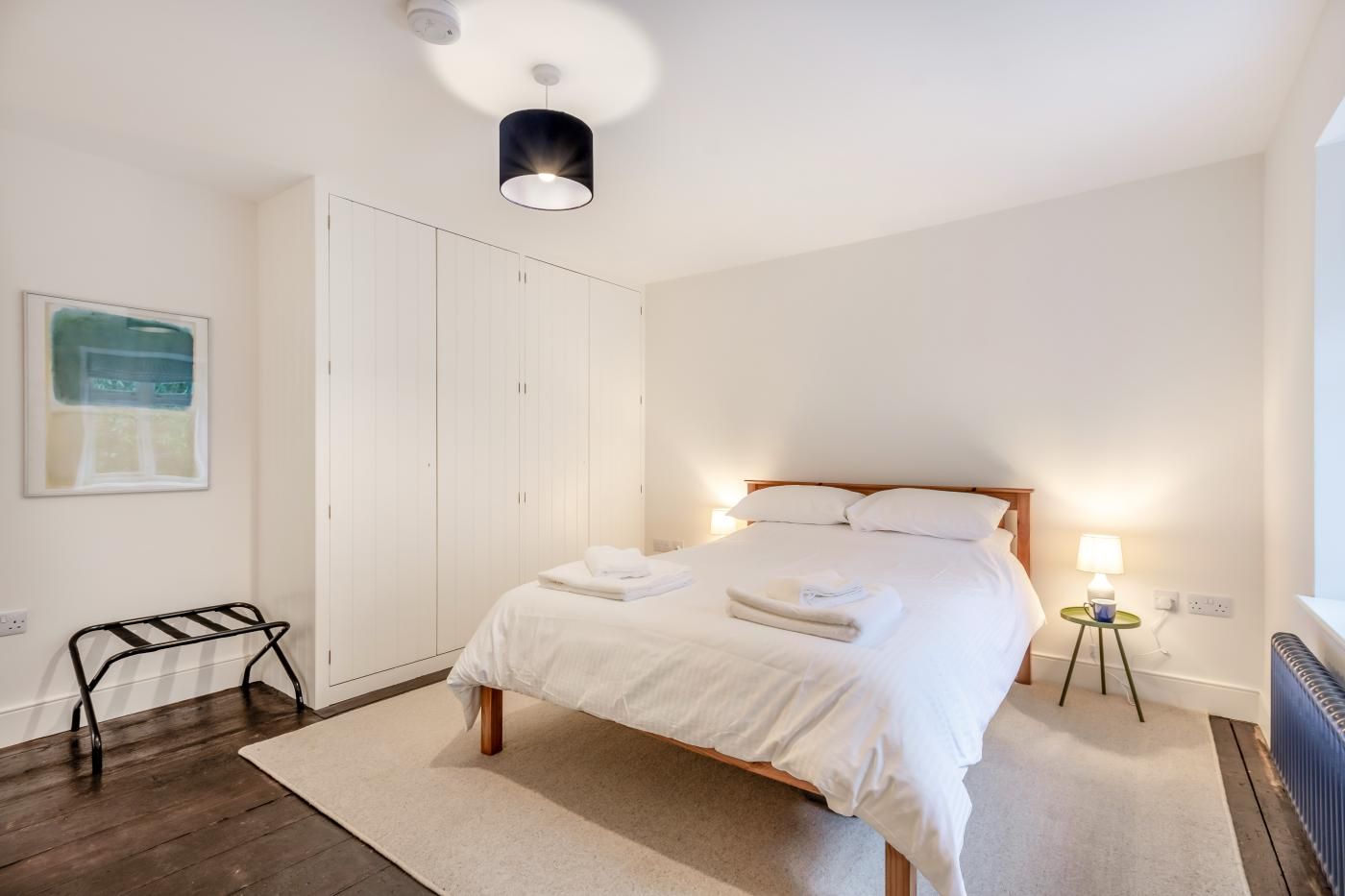 A bedroom with a bed, bedside lamps, a radiator, a wardrobe, and a framed picture on the wall.
