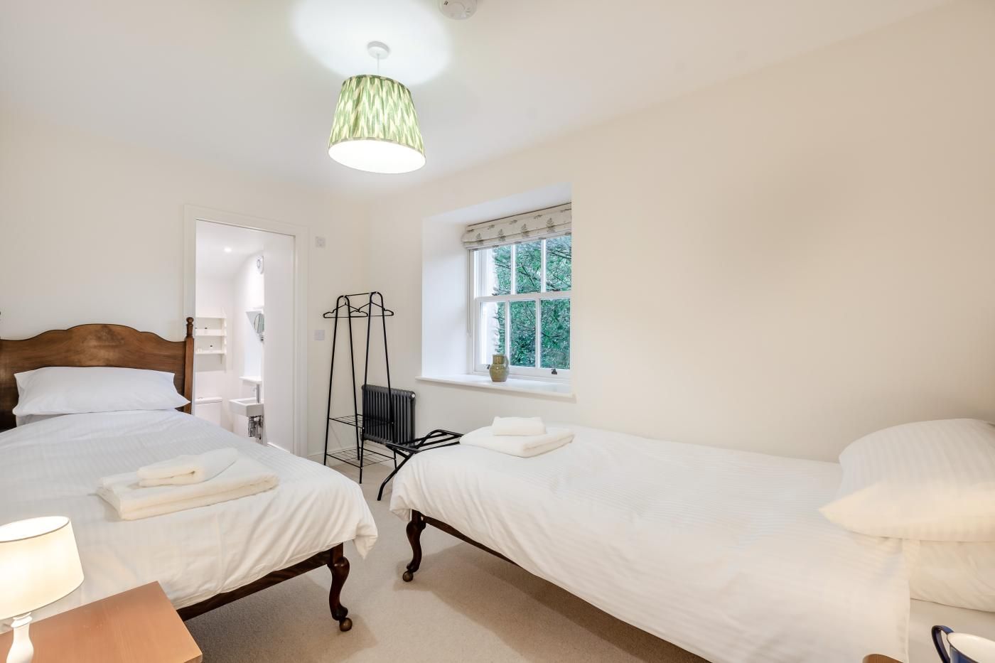 A bedroom with two beds, a radiator, a window with a view, and a hanging light fixture.
