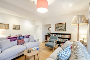 A living room with a sofa, armchair, coffee table, bookshelf, and a lamp. - 5 Bed in Ulpha (oc-b32731) (Ulpha)