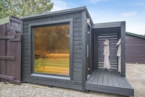 Une petite cabane en bois sombre, dotée d’une grande fenêtre en verre et d’une terrasse en bois.