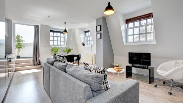 A modern living room with a grey sofa, a dining area, and a TV. - 1 Bed in Brighton (oc-bbnest) (Hove)