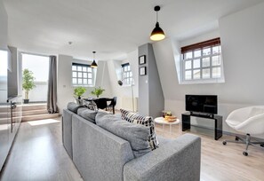 A modern living room with a grey sofa, a dining area, and a TV. - 1 Bed in Brighton (oc-bbnest) (Hove)