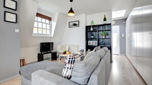 A modern living room with a grey sofa, a TV, a white chair, and a bookshelf. - 1 Bed in Brighton (oc-bbnest) (Hove)