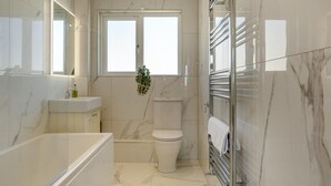 Une salle de bain moderne équipée d’une baignoire, de toilettes et d’une douche à parois de verre.