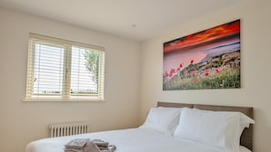 Une chambre à coucher avec un lit, un radiateur, une fenêtre avec des stores et un tableau accroché au mur.