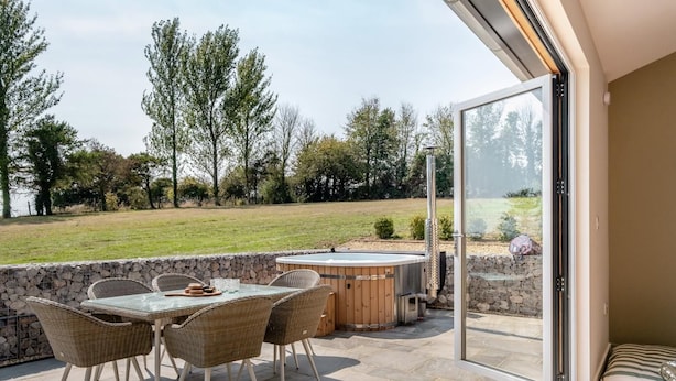 Une terrasse ext érieure avec une porte vitrée donnant accès à une chambre, un jacuzzi et un mur en pierre.