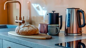 Una encimera de cocina con hogaza de pan, cafetera, hervidor y taza.