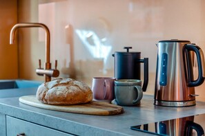 A kitchen counter with a loaf of bread, a coffee maker, a kettle, and a mug.