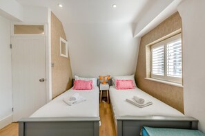 A compact room with two beds, a small table, and a window with blinds. - 3 Bed in Brighton (oc-bbcorn) (Brighton)
