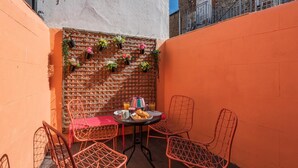 Un pequeño espacio al aire libre para comer, con pared de ladrillo, sillas de metal y una mesa servida con comida y bebidas.