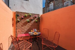 A small outdoor dining area with a brick wall, metal chairs, and a table set with food and drinks.