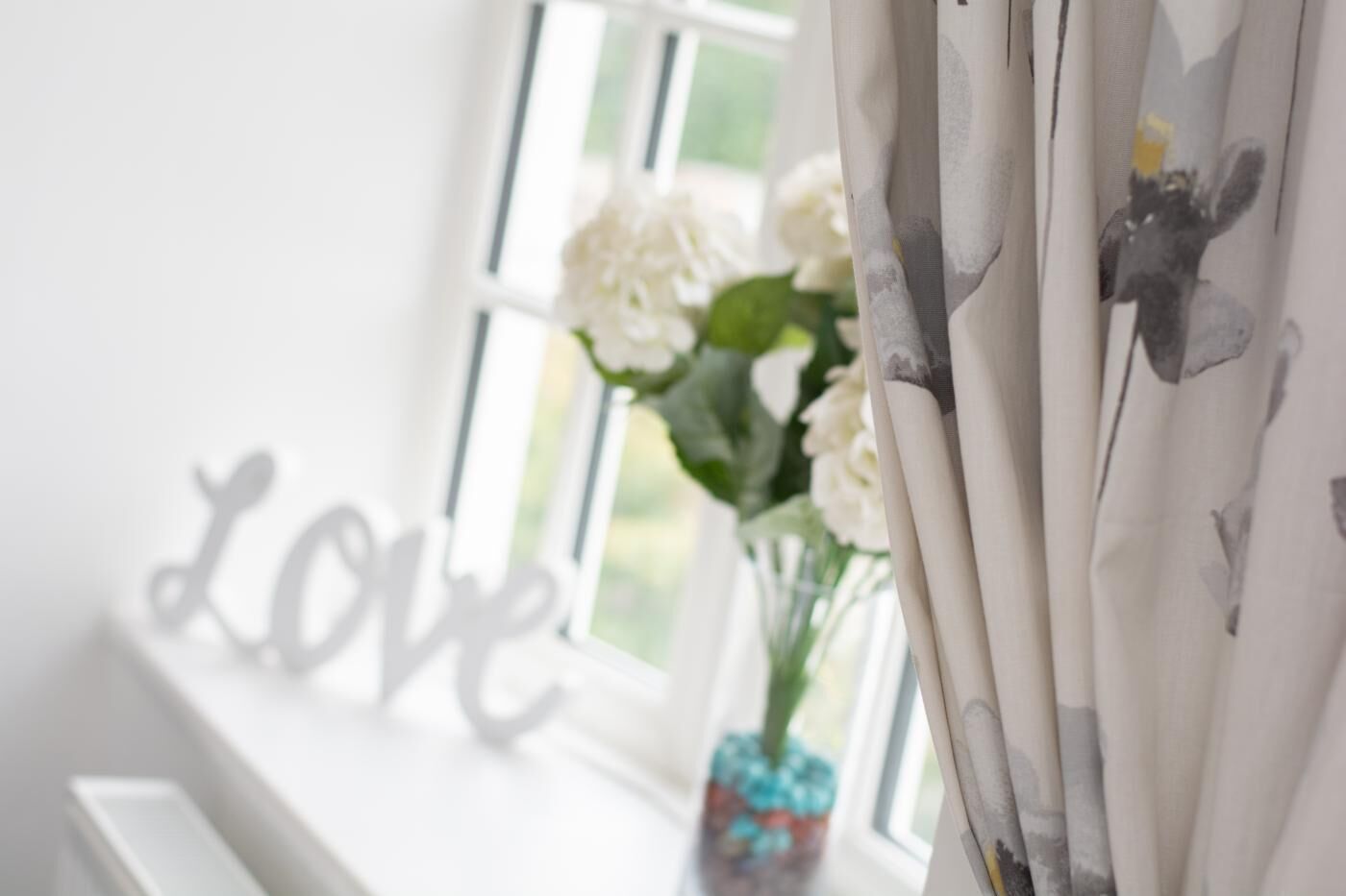 Ein Fenster mit weißen Vorhängen und einer Vase mit weißen Blumen.