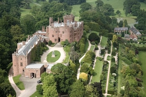 A large castle with a central courtyard, surrounded by manicured gardens and a golf course. - 3 Bed in Forden (oc-c30173) (Forden)